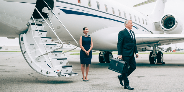 A corporate executive carrying a briefcase while disembarking a private business jet on the tarmac.