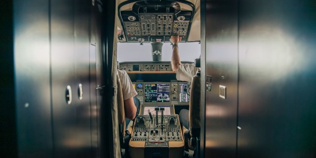 Pilot and copilot reviewing instrument panel controls in a modern aircraft cockpit.