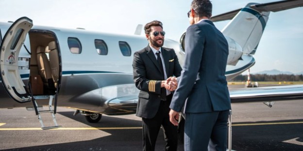 Pilot in uniform shaking hands with a businessman beside a private jet on a tarmac.