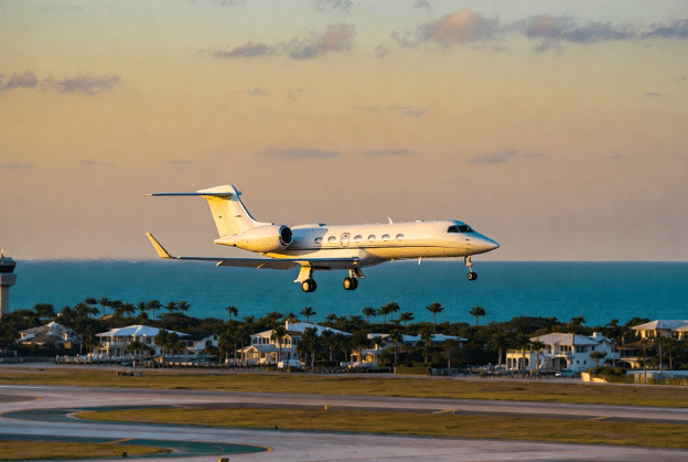Private jet landing at Palm Beach airport during golden hour with the ocean in the background.