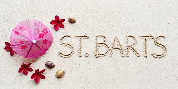 St. Barts written in the sand with a pink umbrella and flowers.