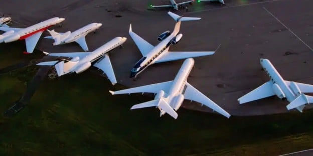 A line up of different sizes of private jets parked together on an airport tarmac.